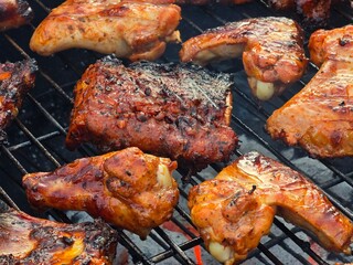 A close-up shot of marinated pork ribs and chicken pieces cooking on a hot barbecue grill with smoky char marks.
