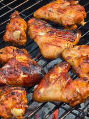 Several chicken wings with crispy, charred skin are cooking on a hot grill over glowing coals, ready to be enjoyed.
