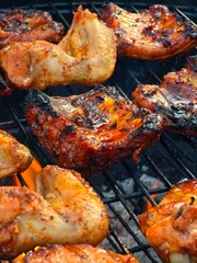A close-up shot of marinated pork ribs and chicken pieces cooking on a hot barbecue grill with smoky char marks.
