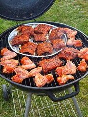 A variety of raw, marinated chicken wings and pork ribs are arranged on a black charcoal grill, ready to be cooked for a delicious barbecue.