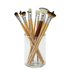 Assorted artist's paintbrushes with polished wooden handles, shiny metal ferrules, diverse natural and synthetic bristles, new and pristine, arranged in a clear glass jar on a transparent studio