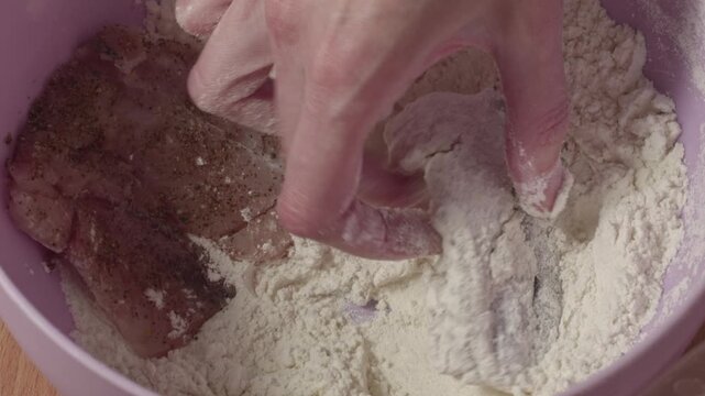 Close-up of woman coating raw hake fish pieces in flour before cooking, recorded with ambient sound.