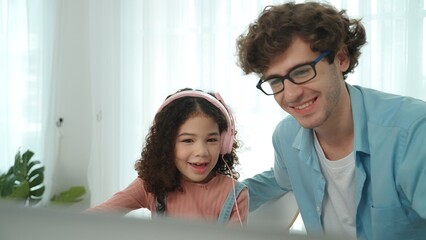 Caucasian dad put headphones on daughter while girl learning code. Father take care schoolgirl while teaching writing engineering prompt and generate Ai by using laptop. Online learning. Pedagogy.