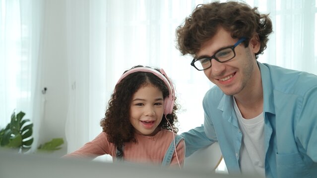 Caucasian dad put headphones on daughter while girl learning code. Father take care schoolgirl while teaching writing engineering prompt and generate Ai by using laptop. Online learning. Pedagogy.