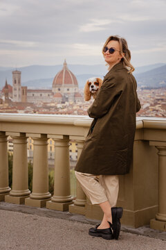 Stylish woman holding a Cavalier King Charles Spaniel on a scenic terrace overlooking the Florence skyline with the iconic Duomo cathedral in the background
