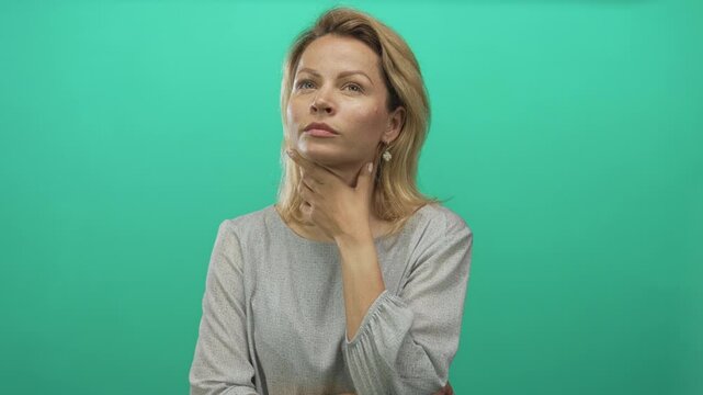 Woman touches chin in green studio while tilting head upward with thinking gesture and steady gaze; curiosity.