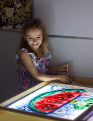 Beautiful little girl draws with sand on a light square, art therapy, sand animation, creative leisure for children, selective focus
