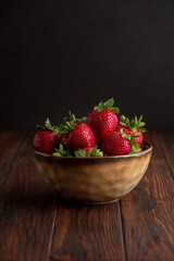 Fresh red strawberries in a rustic bowl on a dark wooden background. Front view