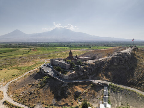 Aerial view of the majestic Khor Virap Monastery perched atop a rugged hill, with the snow-capped peaks of Mount Ararat rising in the distance, Khor Virap, Ararat Province, Armenia.