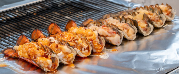 Halved lobster tails are being grilled with cheese. Popular Korean street food, seafood is often enjoyed barbecued or grilled.