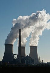 A power station with multiple chimneys emitting white smoke into a clear blue sky, illustrating industrial activity and environmental impact