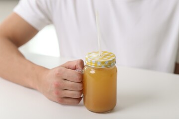 Man with mason jar of orange juice at white table indoors, closeup. Refreshing drink