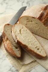 Pieces of fresh bread and knife on white marble table, closeup