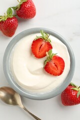 Delicious yogurt in bowl, strawberries and spoon on white marble table, flat lay