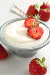 Delicious yogurt in bowl and strawberries on white table, closeup