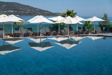 White umbrellas with shadows around outdoor luxury swimming pool 