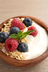 Tasty yogurt with granola and berries in bowl on wooden table, closeup