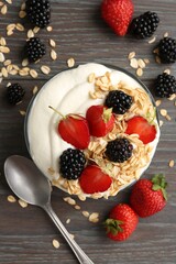 Tasty yogurt with granola and berries in bowl on wooden table, flat lay