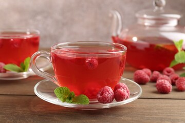 Tasty raspberry tea in glass cups, teapot, berries and mint on wooden table, closeup