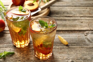 Refreshing iced peach tea in glasses and fresh fruits on wooden table, closeup. Space for text