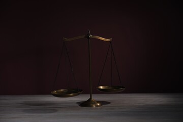 Scales of justice on wooden table against dark background