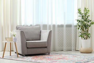 Stylish furniture and houseplant near window with curtains in living room. Interior design