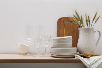 Different clean white dishware, cutlery, cutting board, glasses and spikes on wooden table indoors