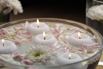 Burning candles, flower and petals in bowl of water on blurred background, closeup