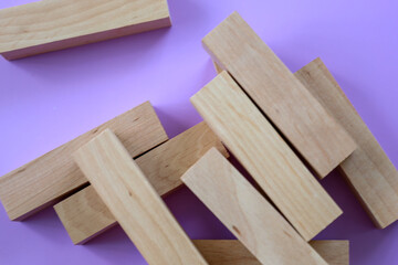 Wooden blocks are scattered randomly on a vibrant lilac background, creating an interesting composition. The natural texture of the light wood contrasts with the rich, solid color, giving the shot a m