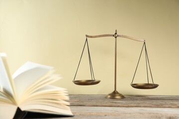 Golden scales of justice and book on wooden table against beige background, selective focus