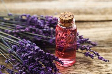 Lavender essential oil in bottle and flowers on wooden table, closeup