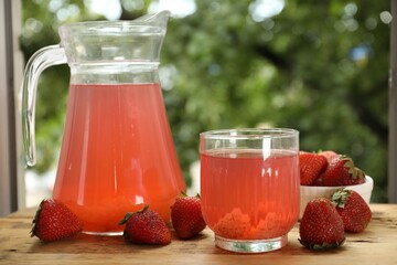 Tasty compot in glass, jug and fresh strawberries on wooden table outdoors