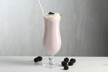 Tasty blackberry milkshake with whipped cream in glass and berries on white marble table