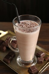 Tasty milkshake in glass and pieces of chocolate on wooden table, closeup