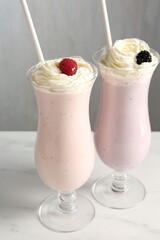 Different tasty milkshakes with whipped cream in glasses and berries on white marble table