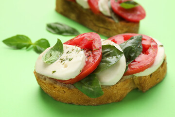 Delicious sandwiches with mozzarella cheese, tomatoes and basil on green background, closeup