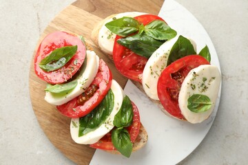 Delicious sandwiches with mozzarella cheese, tomatoes and basil on light grey textured table, top view