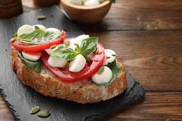 Delicious sandwich with mozzarella cheese, tomatoes and basil on wooden table, closeup