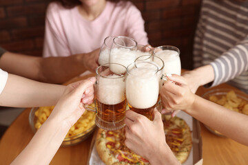 Group of friends clinking glasses of beer at table indoors, closeup