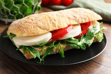 Delicious sandwich with mozzarella cheese, tomato and arugula on wooden table, closeup