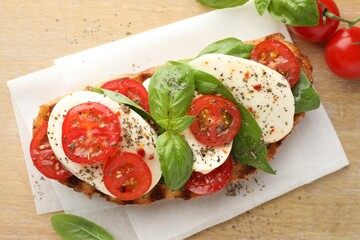 Delicious sandwich with mozzarella cheese, tomatoes and basil on wooden table, flat lay