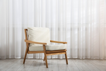 Comfortable beige armchair near window with curtains indoors