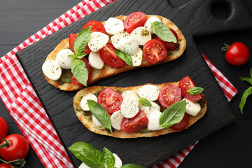 Delicious sandwiches with mozzarella cheese, tomatoes and basil on black wooden table, flat lay