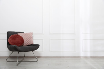 Comfortable armchair with cushions near white wall indoors, space for text