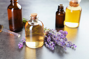Aromatic essential oil in bottles, lavender flowers and dropper on grey textured table, closeup