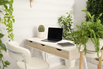 Stylish workplace with laptop, stationery and floral decor in office. Biophilic interior design