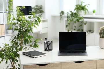 Stylish workplace with laptop, stationery and floral decor in office. Biophilic interior design