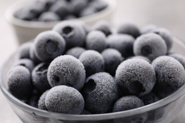 Ripe frozen blueberries in bowl on grey table, closeup