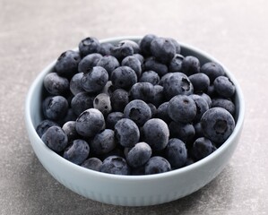 Ripe frozen blueberries in bowl on grey textured table, closeup