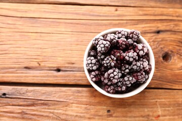 Ripe frozen blackberries in bowl on wooden table, top view. Space for text